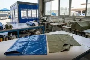 השוואה בין יריעת שמשונית PVC כחולה לבין בד ברזנט ירוק על שולחן עבודה במפעל לייצור כיסויים.